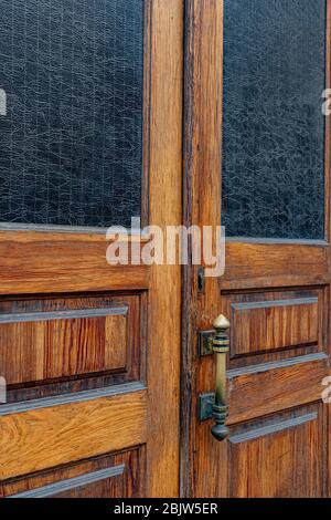 Wooden double door panels with rectangular windows and matte patterned glass inside frames. Brass metal door handle on grunge aged wood texture closeu Stock Photo
