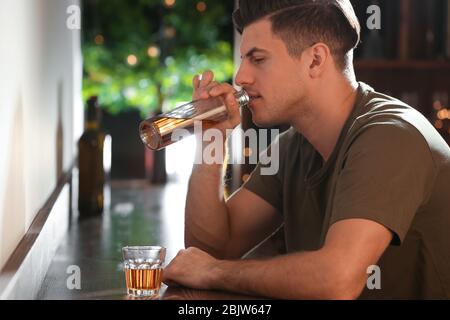 Young man drinking alcohol from bottle in bar Stock Photo