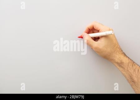 Hand with a marker isolated on gray background. Man holding a red marker against whiteboard, copy space Stock Photo