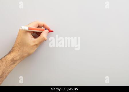 Left hand with a marker isolated on gray background. Left handed man holding a red marker against whiteboard, copy space Stock Photo