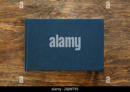 Blank black hardcover book mockup, front side view, Empty closed notebook, branding template on wooden desk background, top view Stock Photo