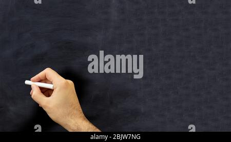 Man hand with a chalk isolated on black background. Teacher holding a white chalk against a chalkboard, copy space Stock Photo