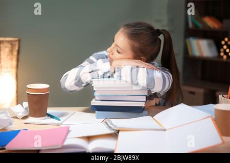 Tired student sleeping on stack of books at table indoors Stock Photo