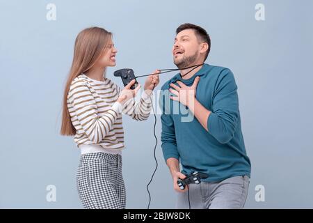 Angry woman strangling her husband with cord from video game controller on color background Stock Photo