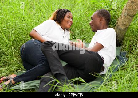 Happy couple lying on green grass laughing and smiling while using the smart phone. Stock Photo
