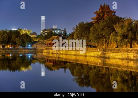 Night view of the corner tower of the Forbidden City Palace Museum and skyscrapers of Central Business District in the distance, reflecting in the wat Stock Photo