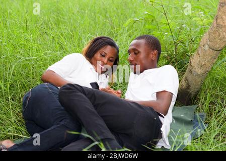 Happy couple lying on green grass laughing and smiling while using the smart phone. Stock Photo