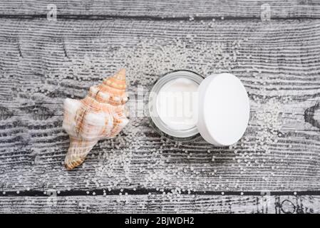 Opened facial cream and sea shell and many tiny salt balls on the wooden background. Nature skin care. Stock Photo
