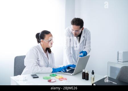 Young researchers or scientists consulting information on a laptop about investigating their samples of Petri dishes in a laboratory. Biochemistry and Stock Photo