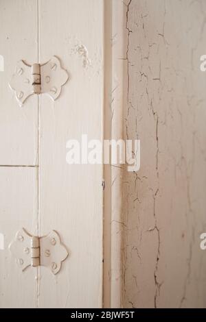 Old door hinges and cracking white paint on an antique furniture. Corner of an ancient dresser with paint cracking and peeling. Stock Photo