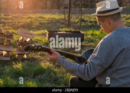 Young man playing acoustic guitar while sitting near campfire. Vacation concept man singing with a guitar on a picnic