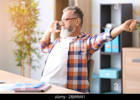 Senior man talking on mobile phone at workplace in office Stock Photo