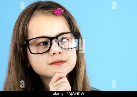 Close up portrait of a cross eyed child school girl wearing looking glasses isolated on blue background. Stock Photo