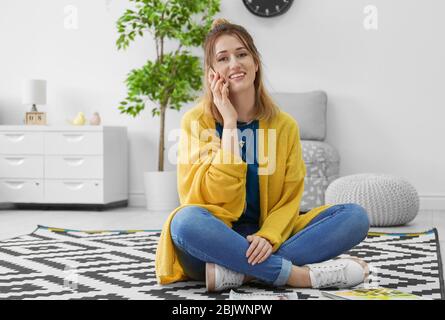 Young woman in yellow cardigan talking on cell phone indoors Stock Photo