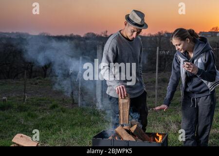 Young friends having fun while preparing for the dinner, standing together near the fire in the backyard Stock Photo