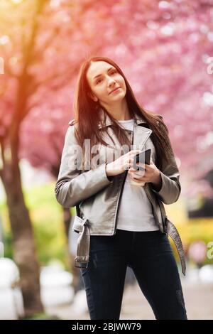 Outdoor portrait of young beautiful fashionable lady posing near flowing tree Stock Photo