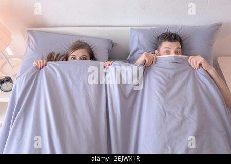 Young couple hiding under blanket on bed at home Stock Photo