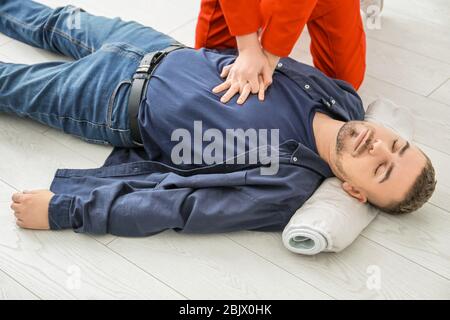 Young woman giving first aid to unconscious man on floor, indoors Stock Photo