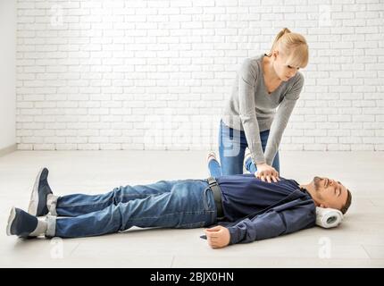 Young woman giving first aid to unconscious man on floor, indoors Stock Photo