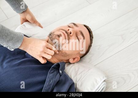 Young woman giving first aid to unconscious man on floor, indoors Stock Photo