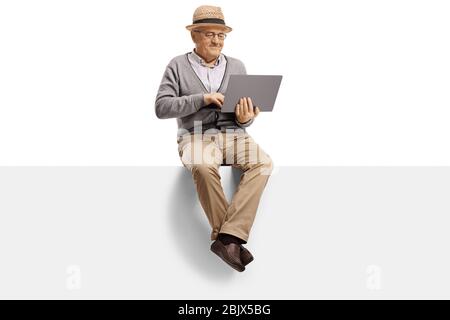 Elderly man sitting on a blank panel and using a laptop computer isolated on white background Stock Photo