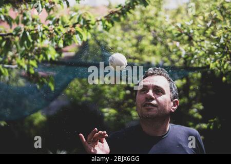 Man in his forties throws and spins a ball that makes water spirals on a green background Stock Photo