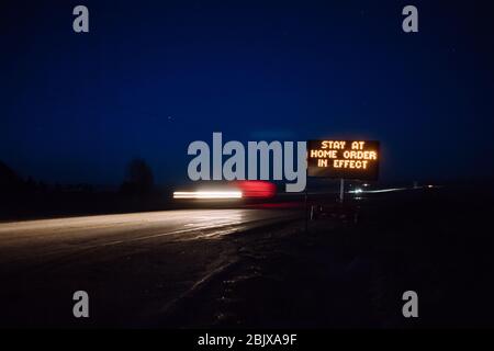 Stay at home order in effect displayed on roadside digital sign at night as cars pass by.  Covid-19 pandemic, stay at home order Stock Photo