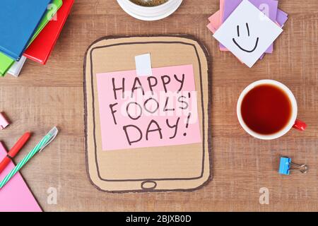 Cardboard tablet computer with phrase 'Happy fool's day' on office table Stock Photo
