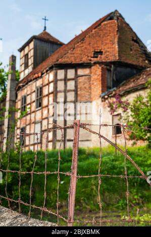 Ruins of the abandoned evangelical church made as half-timbered house with wood and red bricks. Blue sky and green grass and tree. Stock Photo