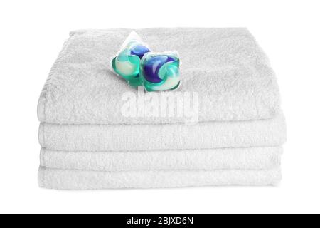Stack of clean folded towels and detergent pods on white background. Laundry day Stock Photo