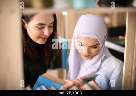 Female student and her Muslim classmate in library Stock Photo