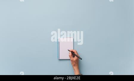 Top view of female hand writing in blank notepad with black marker. Over light blue background with plenty of copy space. Stock Photo