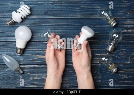 Woman holding LED and incandescent lamp near different light bulbs on wooden background Stock Photo