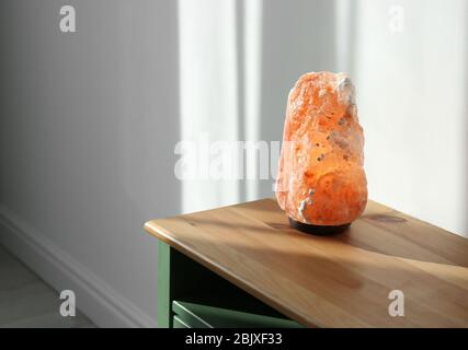 Himalayan salt lamp on wooden cabinet indoors Stock Photo