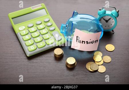 Piggy bank with coins, calculator and alarm clock on table. Pension planning Stock Photo