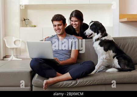 Smilimg couple with dog using a computer laptop at home during corona virus covid 19 lockdown Stock Photo