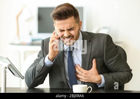 Young businessman calling an ambulance while suffering from heart attack in office Stock Photo