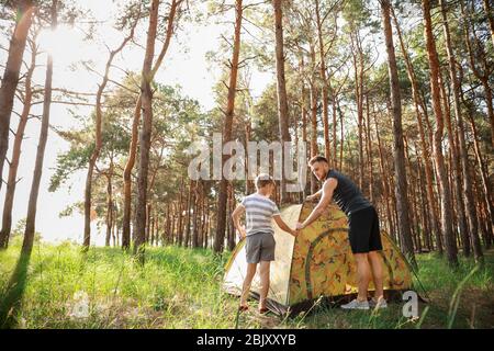 Father and his little son putting up camping tent in forest Stock Photo