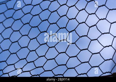 Close-up of a hexagonal cell grating with blue sky in the background. Concepts related to confinement, closure, jail Stock Photo