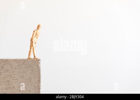 Wooden human figure standing on the edge of a concrete block, looking down. Stock Photo