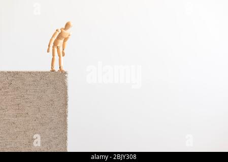 Wooden human figure standing on the edge of a concrete block, looking down. Stock Photo