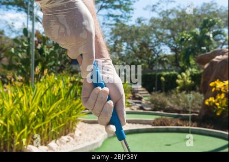 Gloved hands holding a blue mini golf club in the sun Stock Photo