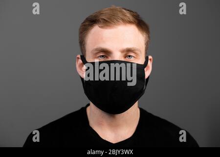 Handsome man in black t-shirt wear black medical mask, gray background. Coronavirus covid-19 quarantine period concept Stock Photo