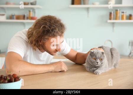 Man with cute funny cat at kitchen table Stock Photo