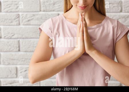 Religious young woman praying against brick wall Stock Photo