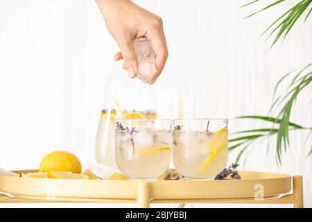 Woman dropping ice cubes into glass of lavender lemonade on table Stock Photo