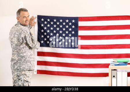 Mature male soldier hanging USA flag on wall in headquarters building ...
