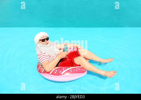 Santa Claus relaxing on inflatable ring in swimming pool Stock Photo