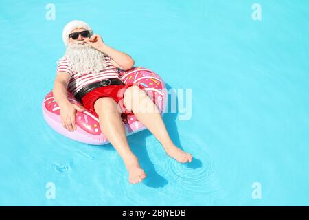 Santa Claus relaxing on inflatable ring in swimming pool Stock Photo