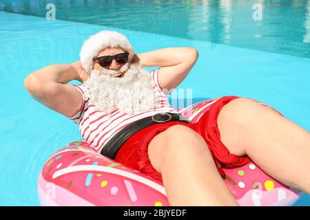 Santa Claus relaxing on inflatable ring in swimming pool Stock Photo